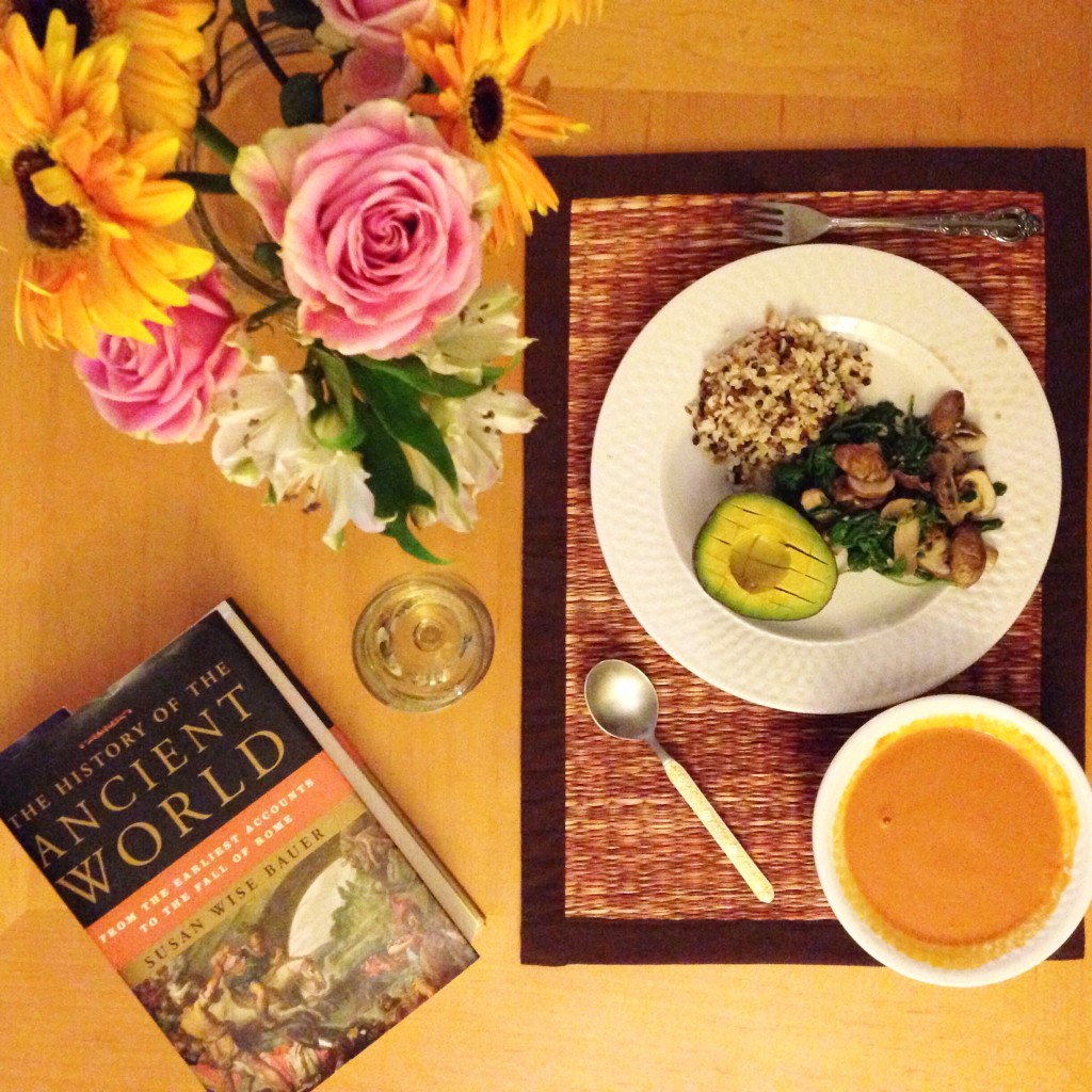 "The History of the Ancient World" book laying on the table next to a dinner spread and a bouquet of flowers.