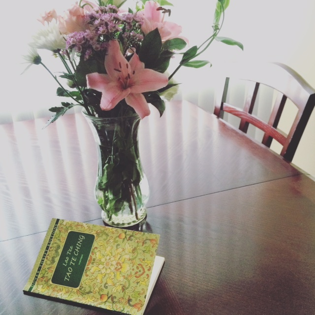 Tao Te Ching book lying on a table next to a vase with a bouquet of flowers